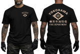 Front and back views of a black short-sleeve t-shirt worn by a model. The front left chest has a small beige Japanese fire department emblem and text.