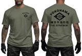 Front and back views of an olive green short-sleeve t-shirt worn by a model. The front features a small black chest graphic, and the back features a large black graphic with the text 'YOKOHAMA', 'FIRE DEPARTMENT', and Japanese characters.
