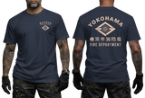 Front and back views of a navy blue short-sleeve t-shirt worn by a model. The front features a small beige chest logo, and the back features a large beige graphic with the text 'YOKOHAMA FIRE DEPARTMENT' and Japanese characters.