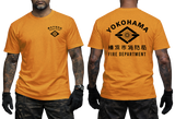 An orange short-sleeve t-shirt shown on a model from both the front and back views. The front features a small black logo on the left chest, and the back features a large black diamond logo with the text 'YOKOHAMA' and 'FIRE DEPARTMENT' in English and Japanese.