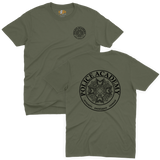 Classic military green t-shirt featuring the Police Academy movie logo with a small left-chest emblem and a large circular back print displaying the badge design with the text POLICE ACADEMY and INTEGRITY KNOWLEDGE COURAGE.