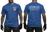 Two-panel photo showing the front and back of a blue short-sleeve t-shirt. The front features a small circular "Antarctic Fire Department McMurdo Station" logo on the left chest. The back displays large white text: "ANTARCTIC FIRE DEPARTMENT McMurdo Station