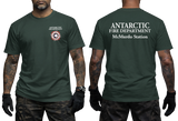 Two-panel photo showing the front and back of a green short-sleeve t-shirt. The front features a small circular "Antarctic Fire Department McMurdo Station" logo on the left chest. The back displays large white text: "ANTARCTIC FIRE DEPARTMENT McMurdo Station