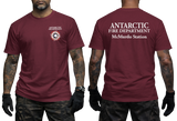 Two-panel photo showing the front and back of a maroon short-sleeve t-shirt. The front features a small circular "Antarctic Fire Department McMurdo Station" logo on the left chest. The back displays large white text: "ANTARCTIC FIRE DEPARTMENT McMurdo Station