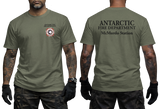 Two-panel photo showing the front and back of a military green short-sleeve t-shirt. The front features a small circular "Antarctic Fire Department McMurdo Station" logo on the left chest. The back displays large white text: "ANTARCTIC FIRE DEPARTMENT McMurdo Station