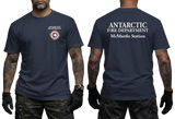 Two-panel photo showing the front and back of a navy short-sleeve t-shirt. The front features a small circular "Antarctic Fire Department McMurdo Station" logo on the left chest. The back displays large white text: "ANTARCTIC FIRE DEPARTMENT McMurdo Station