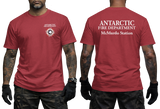 Two-panel photo showing the front and back of a red short-sleeve t-shirt. The front features a small circular "Antarctic Fire Department McMurdo Station" logo on the left chest. The back displays large white text: "ANTARCTIC FIRE DEPARTMENT McMurdo Station