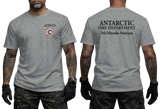 Two-panel photo showing the front and back of a grey short-sleeve t-shirt. The front features a small circular "Antarctic Fire Department McMurdo Station" logo on the left chest. The back displays large white text: "ANTARCTIC FIRE DEPARTMENT McMurdo Station