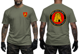 Front and back views of an olive green t-shirt worn by a model. The front features a small red and yellow military crest on the left chest, and the back features a large circular red, yellow, and black graphic with the text 'ARMED FORCES OF MALAYA' and 'FREELAND BELICLAN VENTUS'.