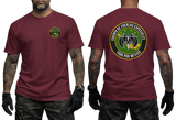 A man modeling a burgundy short-sleeve t-shirt, showing both the front and back views. The front features a small circular green and yellow emblem on the left chest.