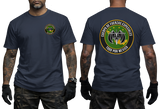 A man modeling a navy blue t-shirt, showing both the front and back views. The front features a small circular green and yellow emblem on the left chest.