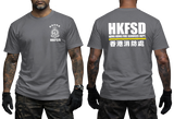 A man modeling a dark gray short-sleeve t-shirt, showing both the front and back views. The front features a white HKFSD emblem on the left chest, and the back features large white text reading 'HKFSD' with 'HUANG KONG FIRE SERVICES DEPT' and Chinese characters below.