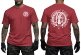 Two-view composite image of a red t-shirt displayed on a male model with tattooed arms and tactical gloves. The left side shows the front of the shirt with a small left-chest logo. The right side shows the back of the shirt with a large, detailed white graphic print of the Saint Benedict Medal and the circular text 'INTERNATIONAL CATHOLIC ASSOCIATION of EXORCISTS'.