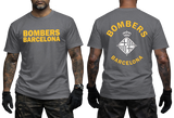 A man modeling a dark gray t-shirt showing both the front and back views. The front features yellow text reading 'BOMBERS BARCELONA', and the back features a large white and yellow graphic with a crown and diamond emblem.
