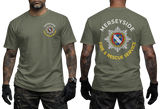 Front and back views of an olive green t-shirt worn by a model. The front left chest features a small circular Merseyside Fire & Rescue Service emblem.